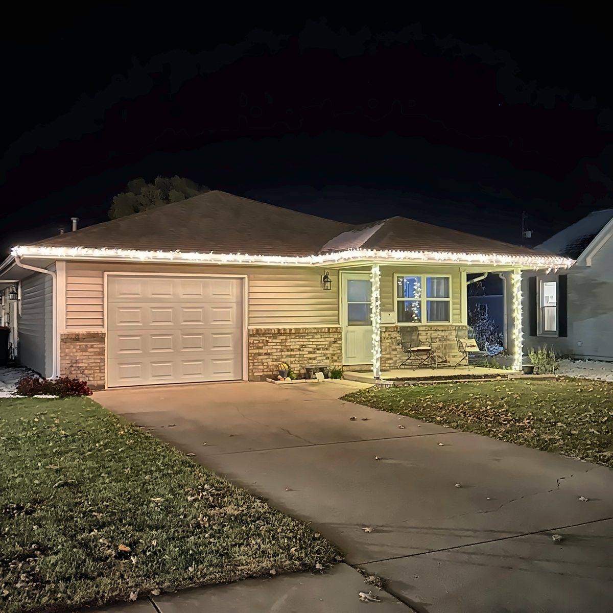 Small ranch home with warm white lights on the gutter line and wrapped porch posts
